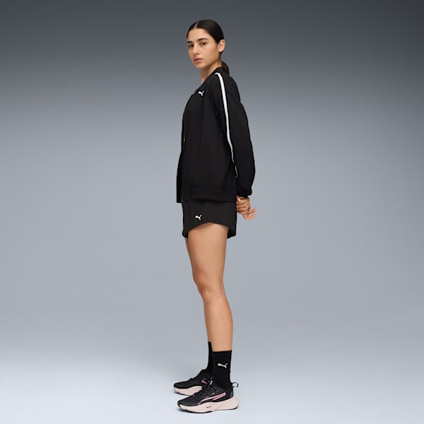 A model stands against a grey backdrop, wearing a black jacket, shorts and running shoes.